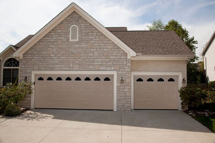 Multiple sandstone raised panel garage doors with top windows on stone veneer house